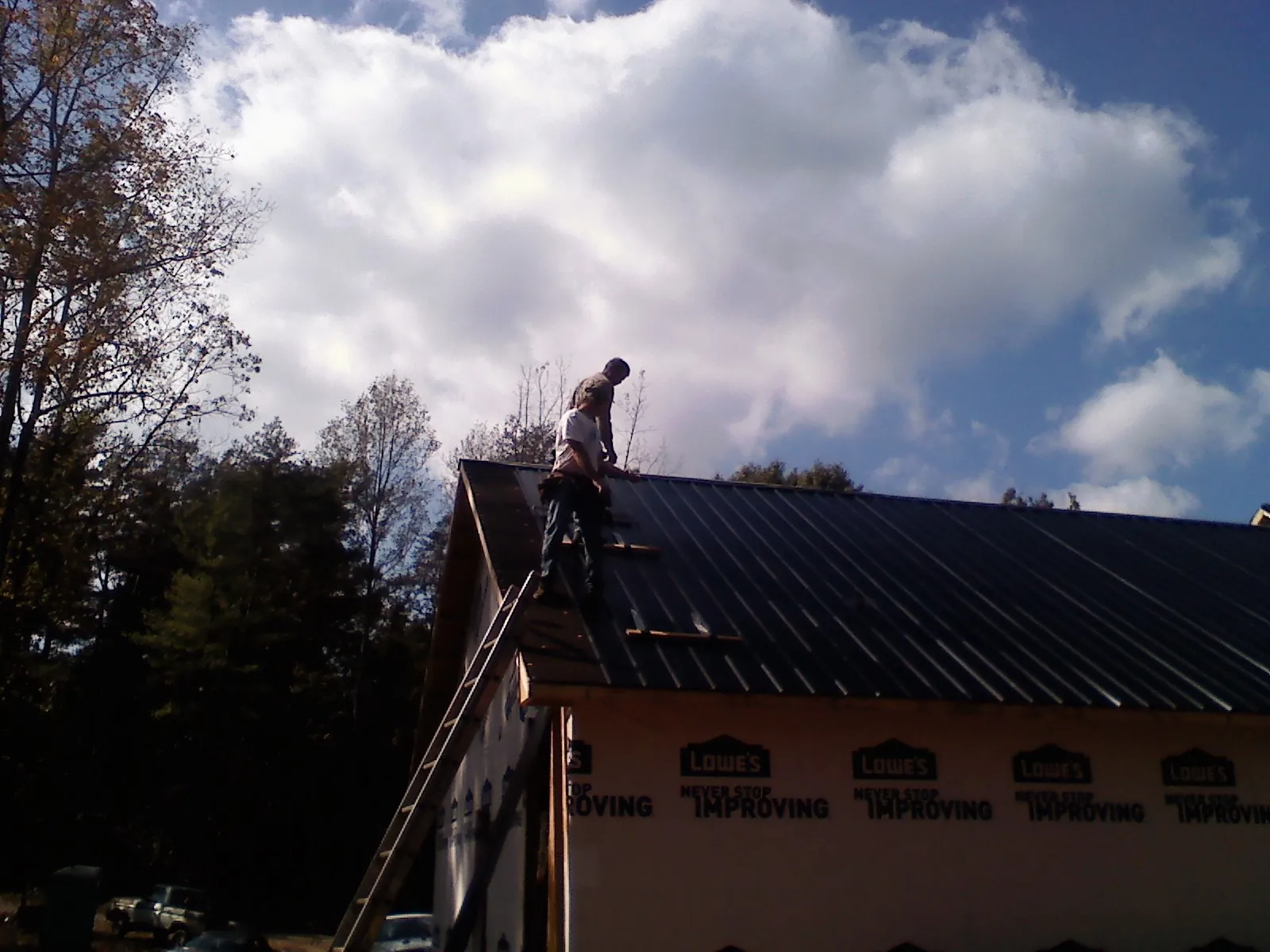 Roofer fastening dark metal panels high against a cloudy sky, from a Roof Inspection job in Thompson