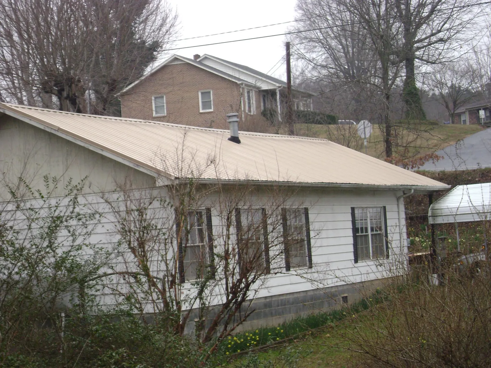 Tan metal roof on a white sided house set into a hillside — Commercial Roofing by Roofing Brothers in Thompson